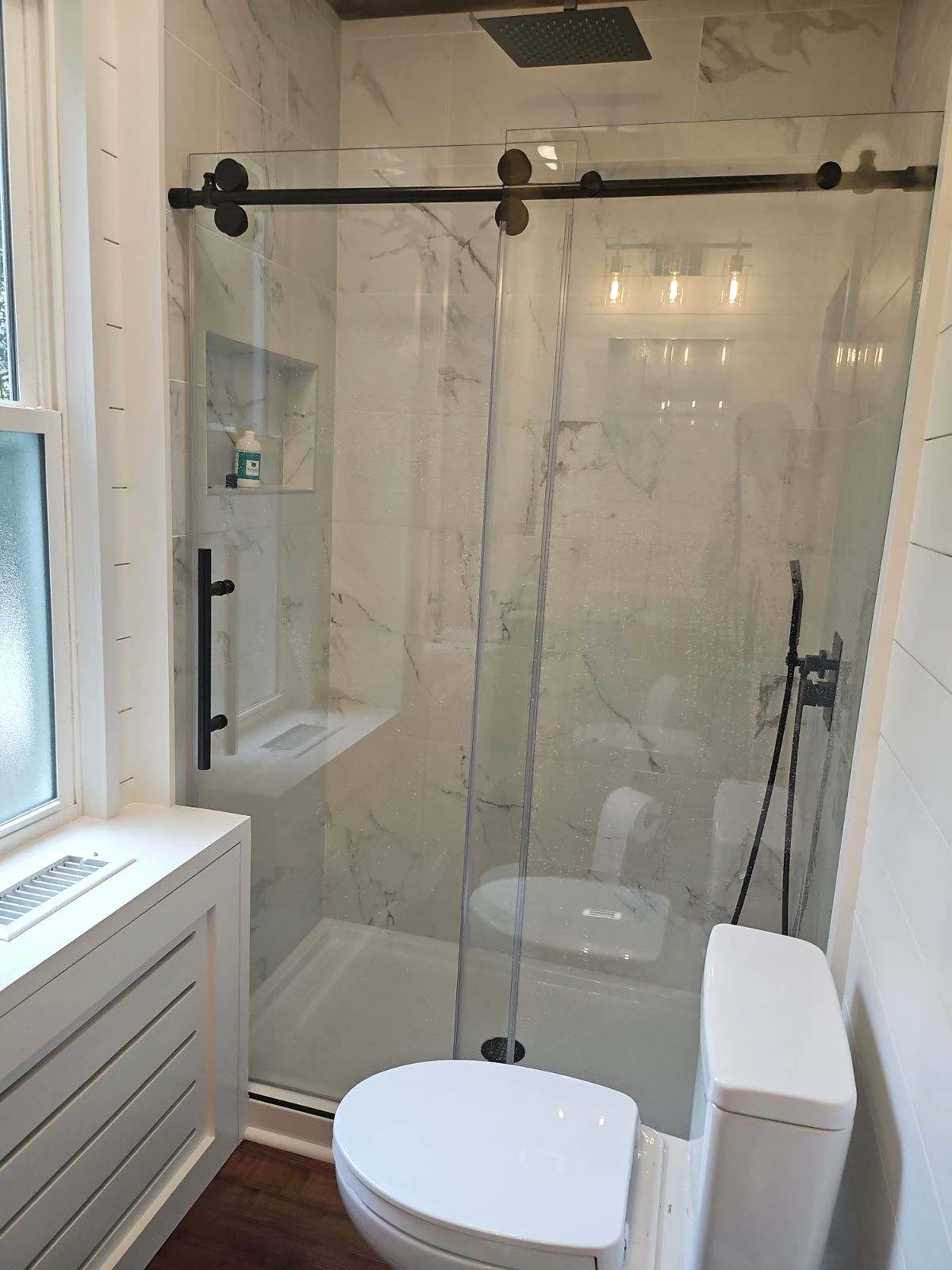 Glass shower enclosure with marble-look tile and black hardware